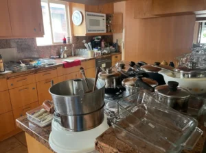 A kitchen with wooden cabinets and countertops, cluttered with various pots, pans, glassware, and utensils.