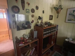Small room with wooden shelves, wall art, a mirror, and various decorative items; bathroom visible through doorway.