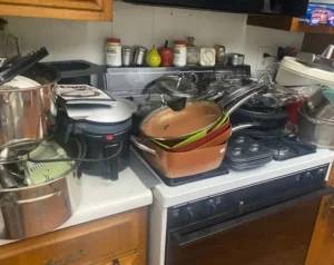 Kitchen counter and stove cluttered with various pots, pans, and cookware, with a toaster oven to the left.