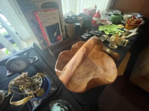 Wooden bowl with handle on a table surrounded by various household items, decor, and small appliances.